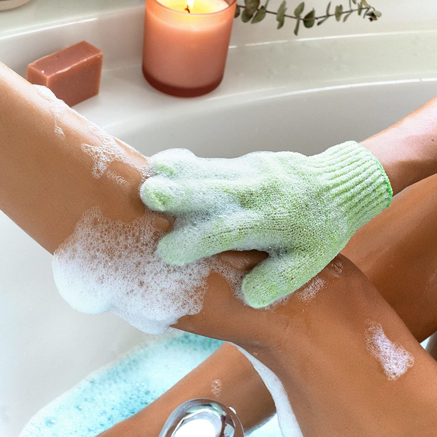 person in the bath scrubbing their leg with the glove