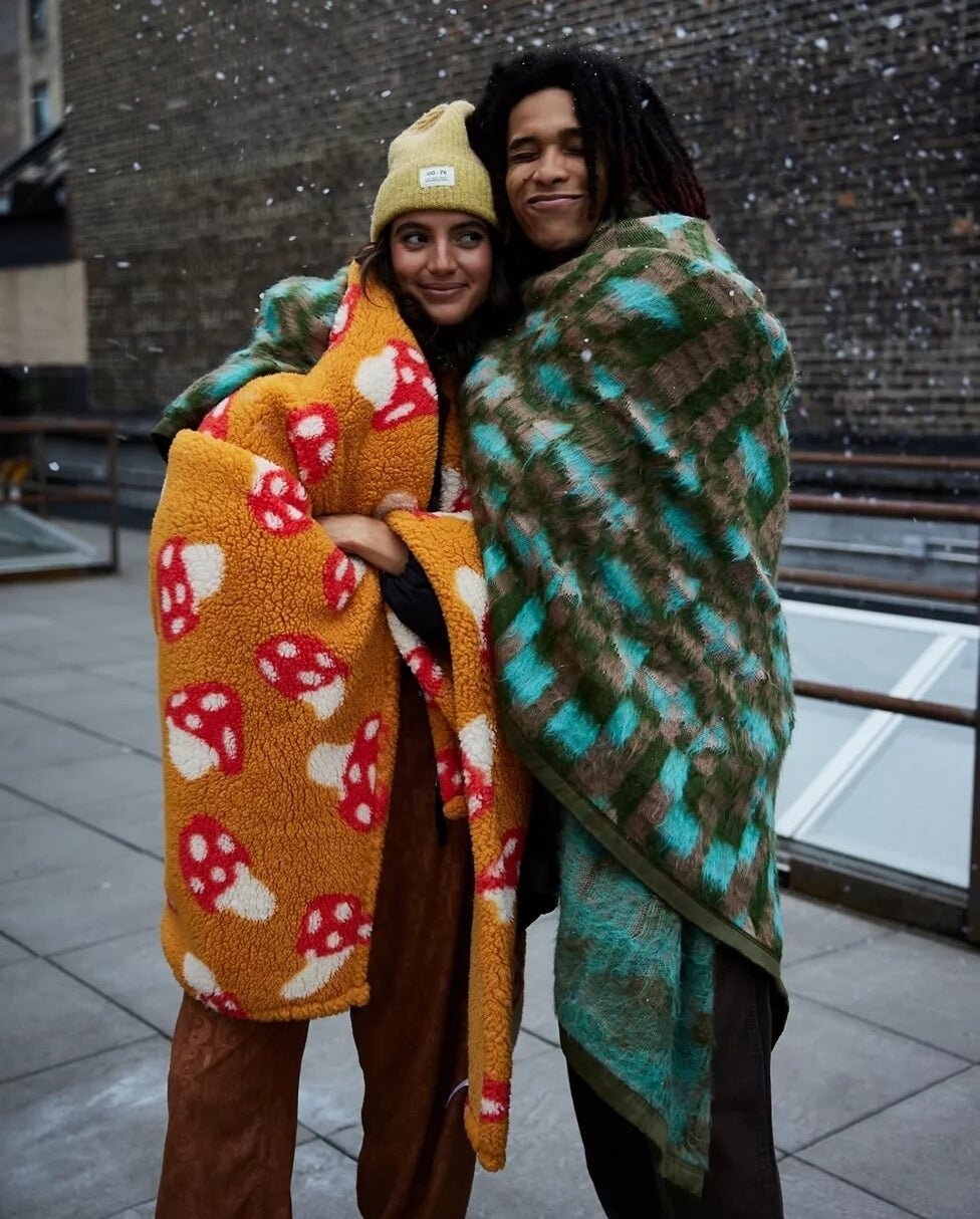 two people outside in the snow with the blankets wrapped around them