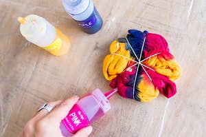 A hand uses a bottle of paint to make a tie-dye shirt