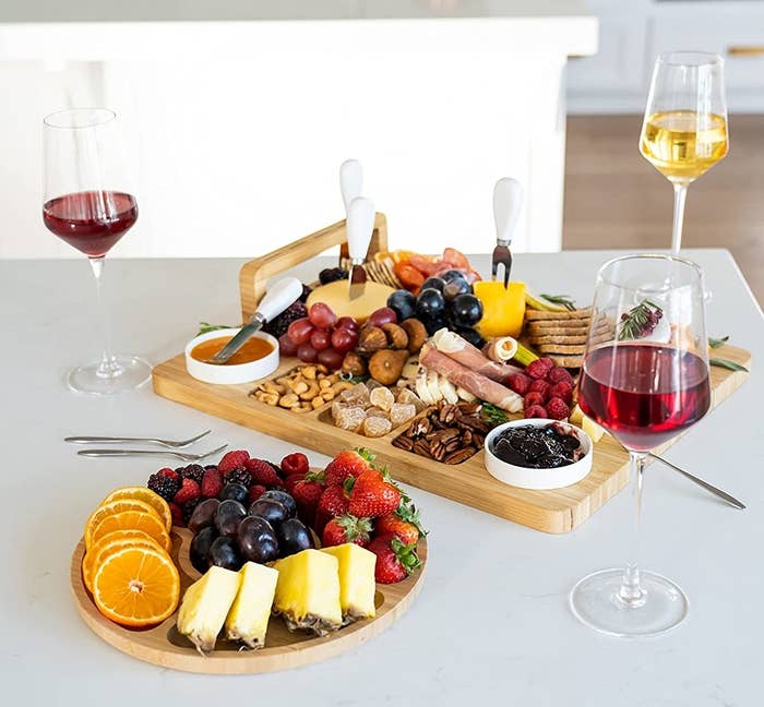 the charcuterie board and fruit tray filled with foods beside wine glasses