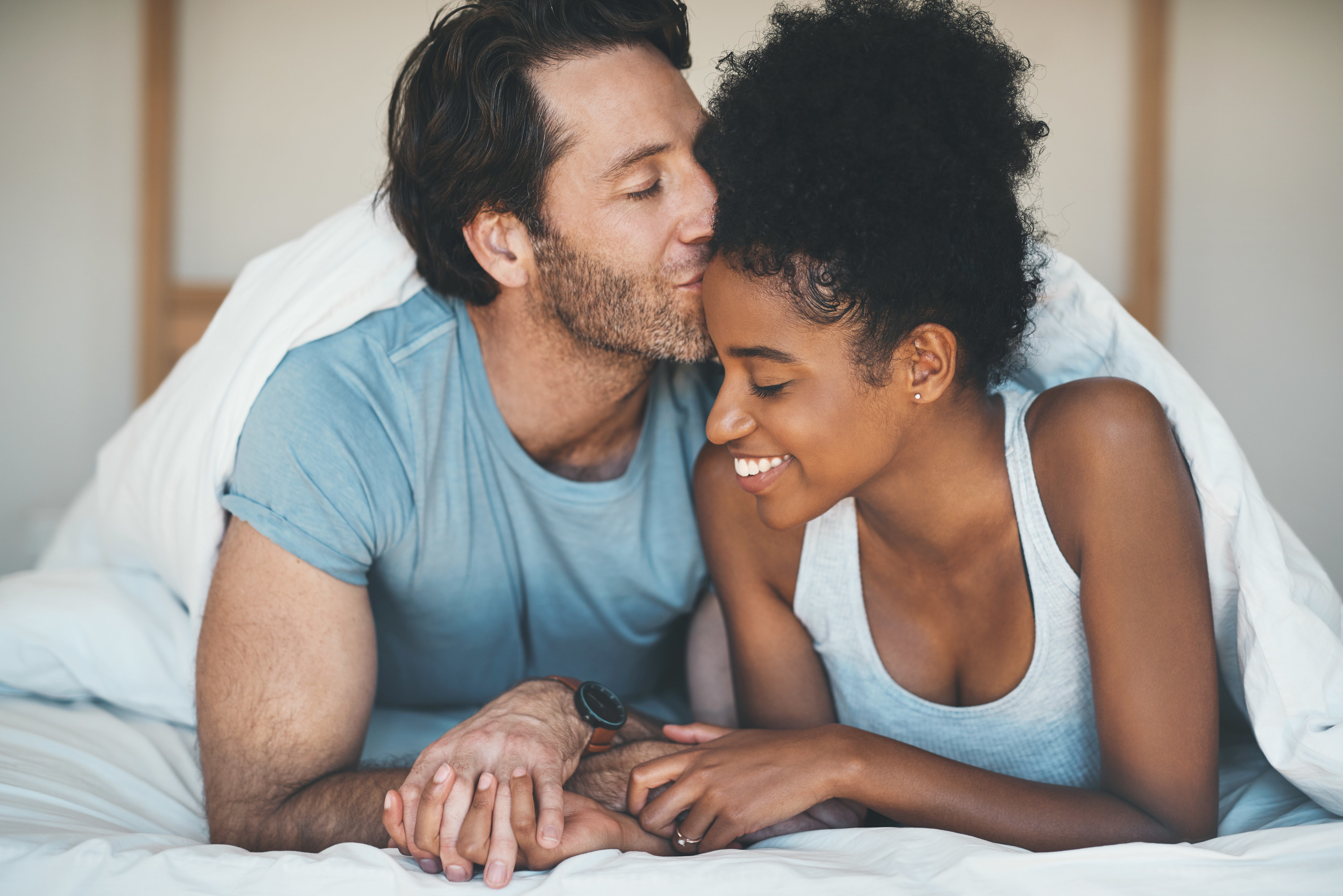 a man kissing a woman&#x27;s forehead in bed