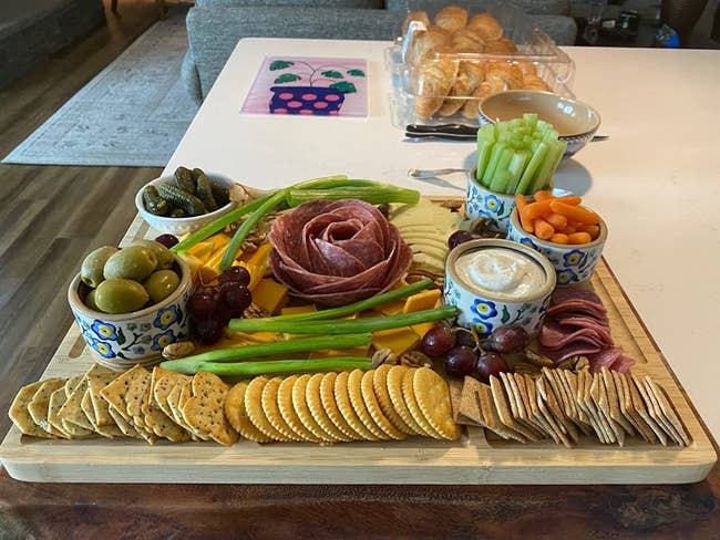 A reviewer's board with crackers in the grooves, and many pieces of cheese, meat, olives, veggies, and more