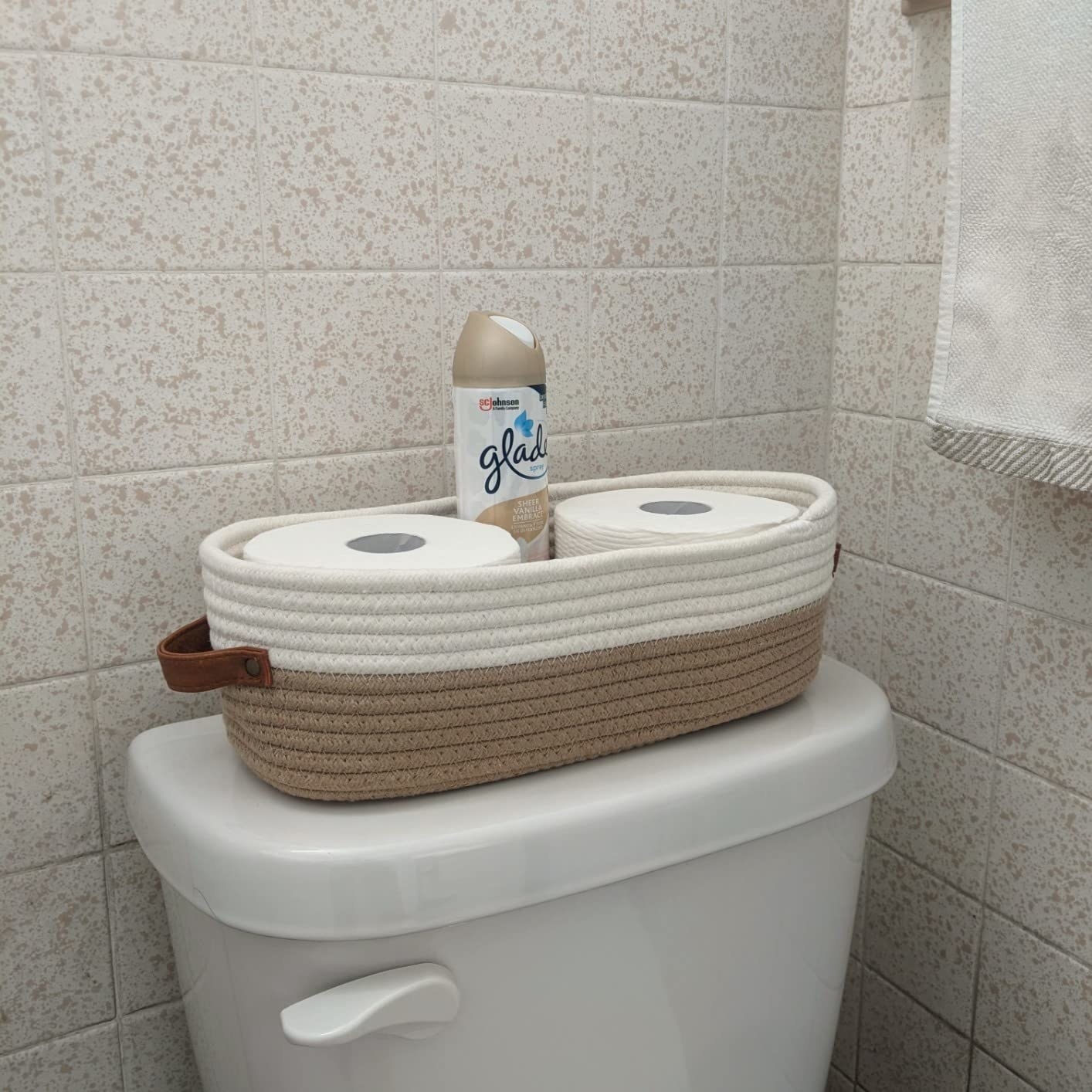 the woven basket with toilet paper and an air freshener on top of a toilet tank