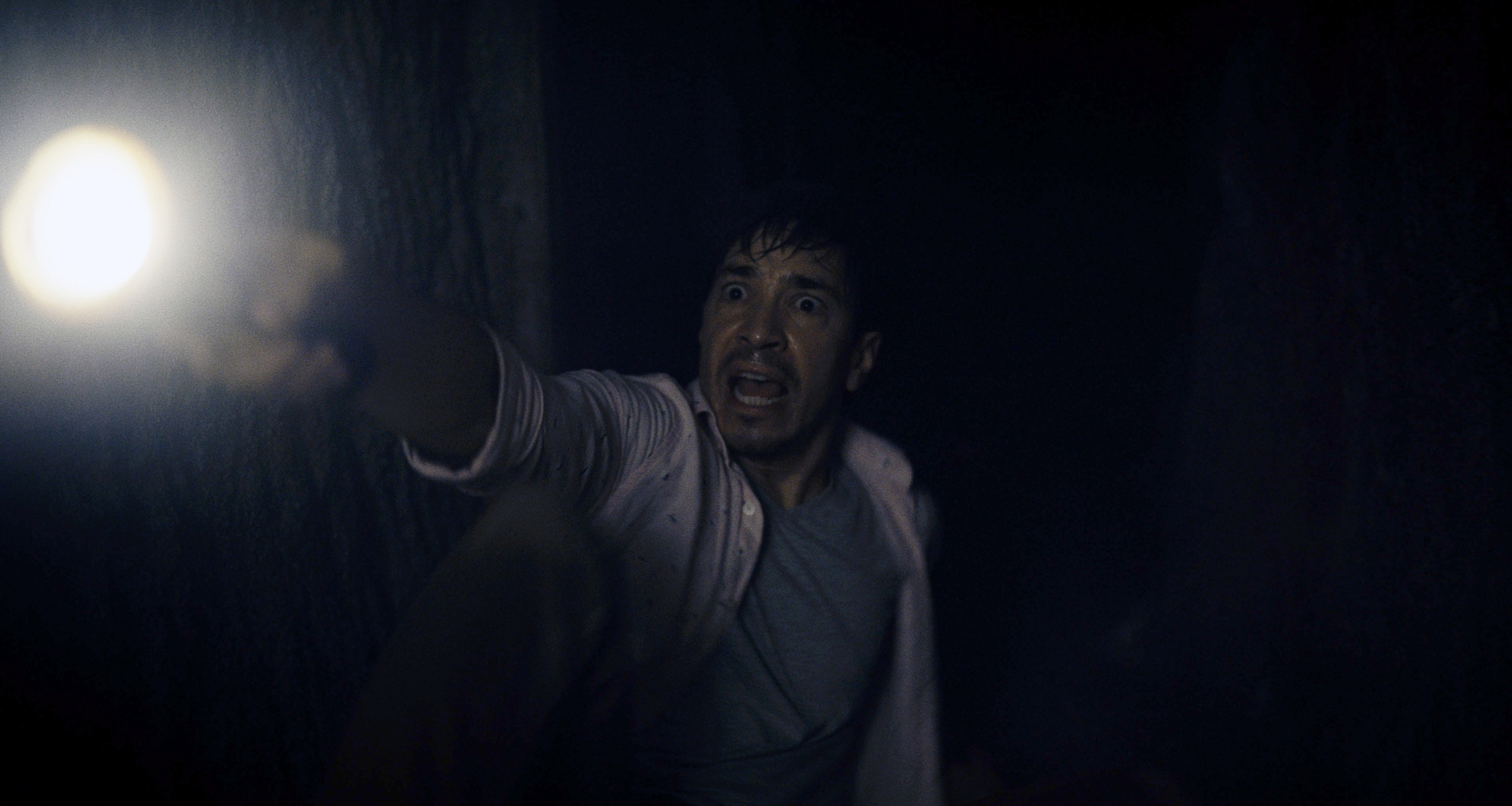 Justin Long screaming in the dark with a flashlight in Barbarian.