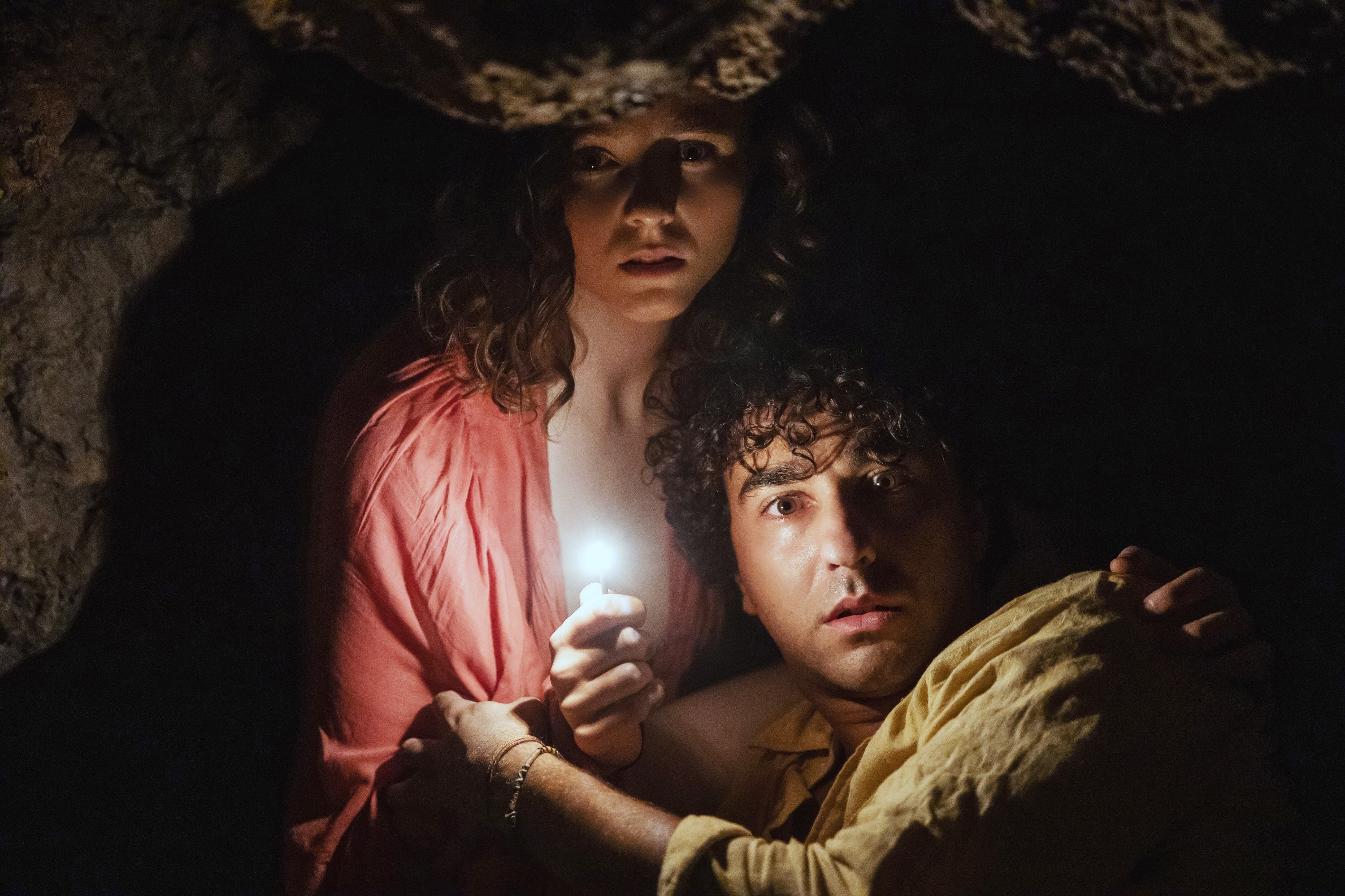 Thomasin McKenzie and Alex Wolff huddled together on a dark beach in Old.