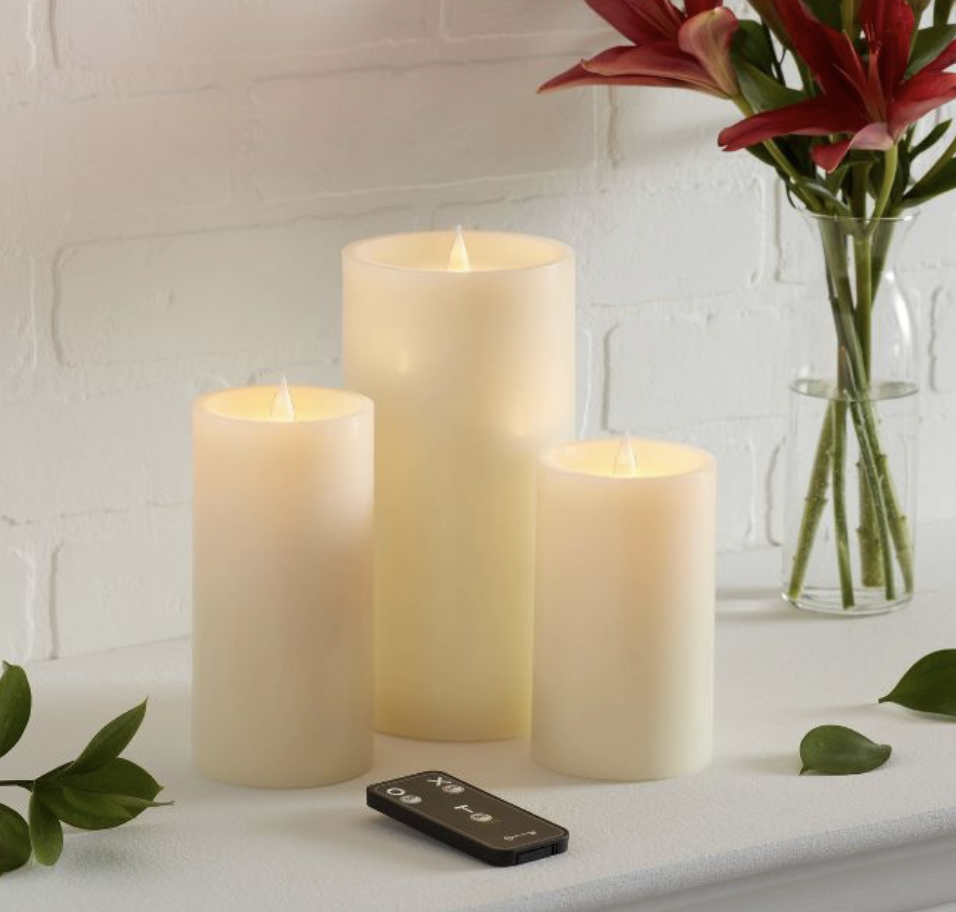 Three battery-operated LED candles on a counter, with a remote control next to them