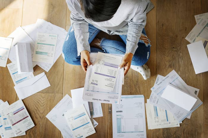 Woman sits on the floor surrounded by bills