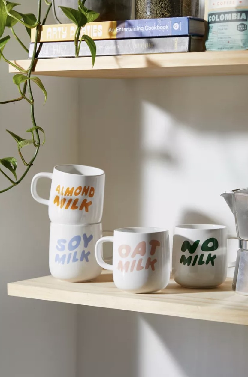 The shelf has &quot;almond milk,&quot; &quot;oat milk,&quot; &quot;soy milk&quot; and &quot;no milk&quot; mugs in fun fonts with differing colors.