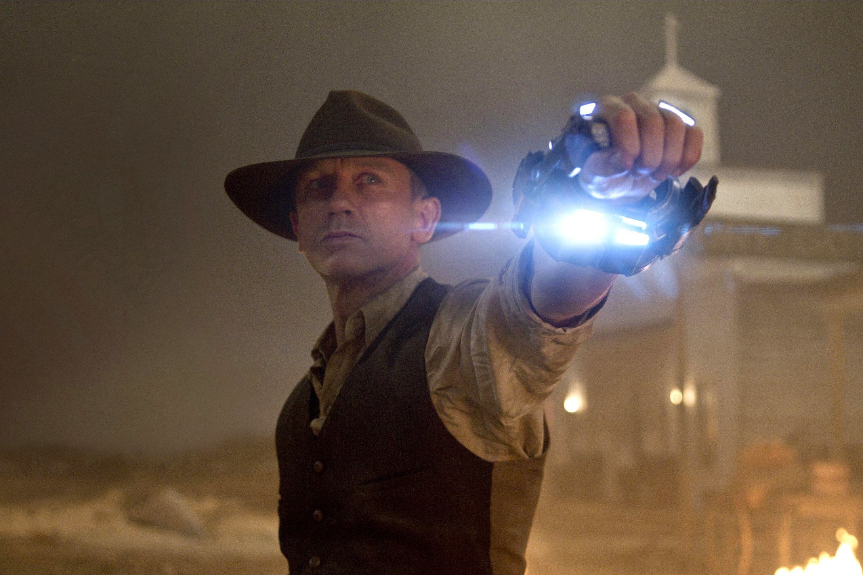 A stoic cowboy holds up a glowing extraterrestrial weapon