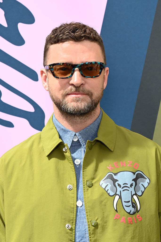 A closeup of Justin at a red carpet event wearing multicolored sunglasses and a Kenzo jacket with an elephant on it