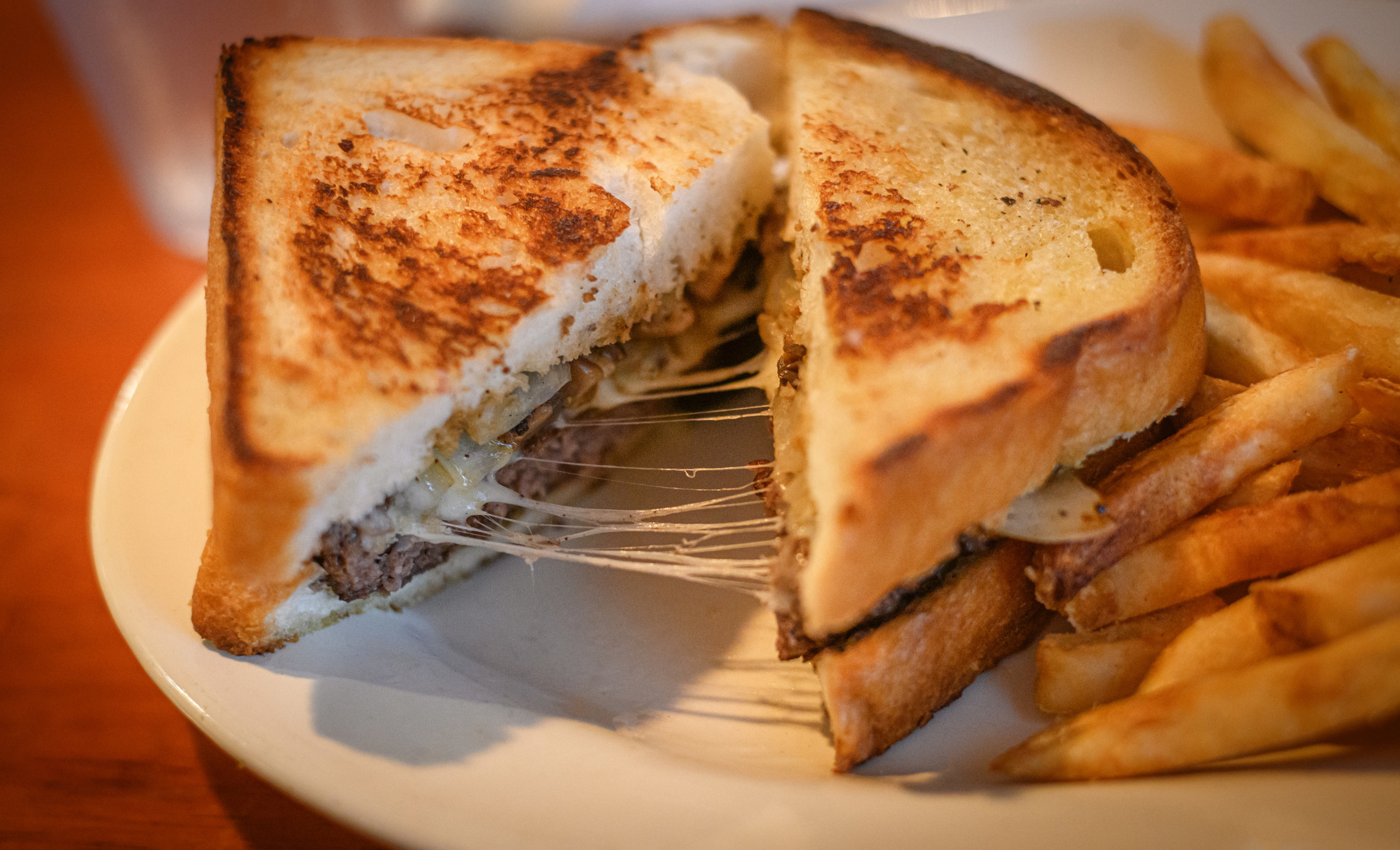 A cheesy patty melt with French fries.
