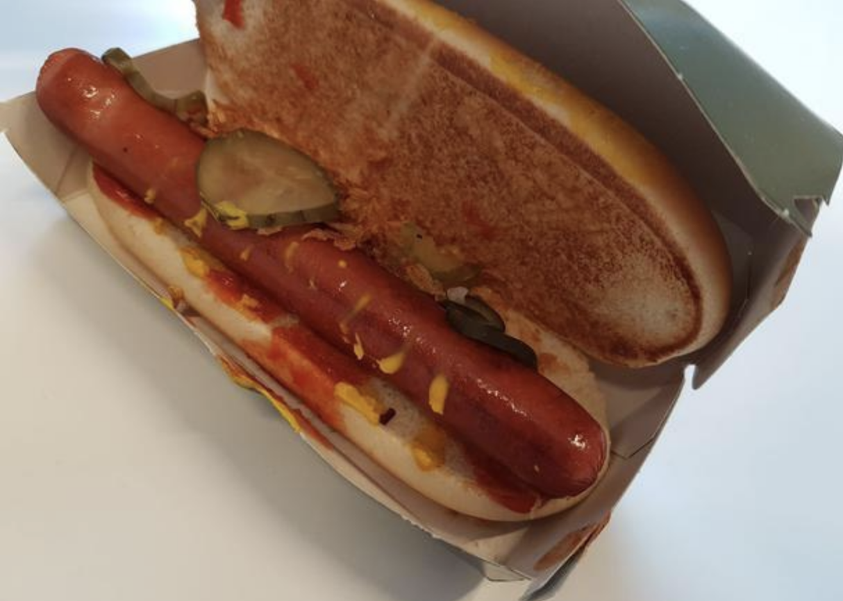 A hot dog in a bun with pickles, ketchup, and cheese