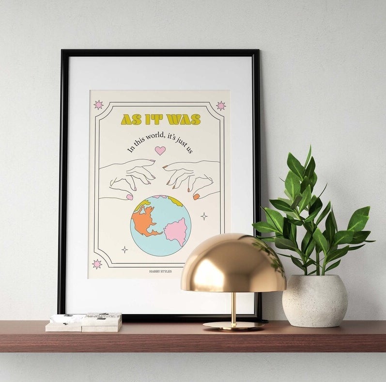 the print in a frame leaning against a wall beside a lamp and a plant