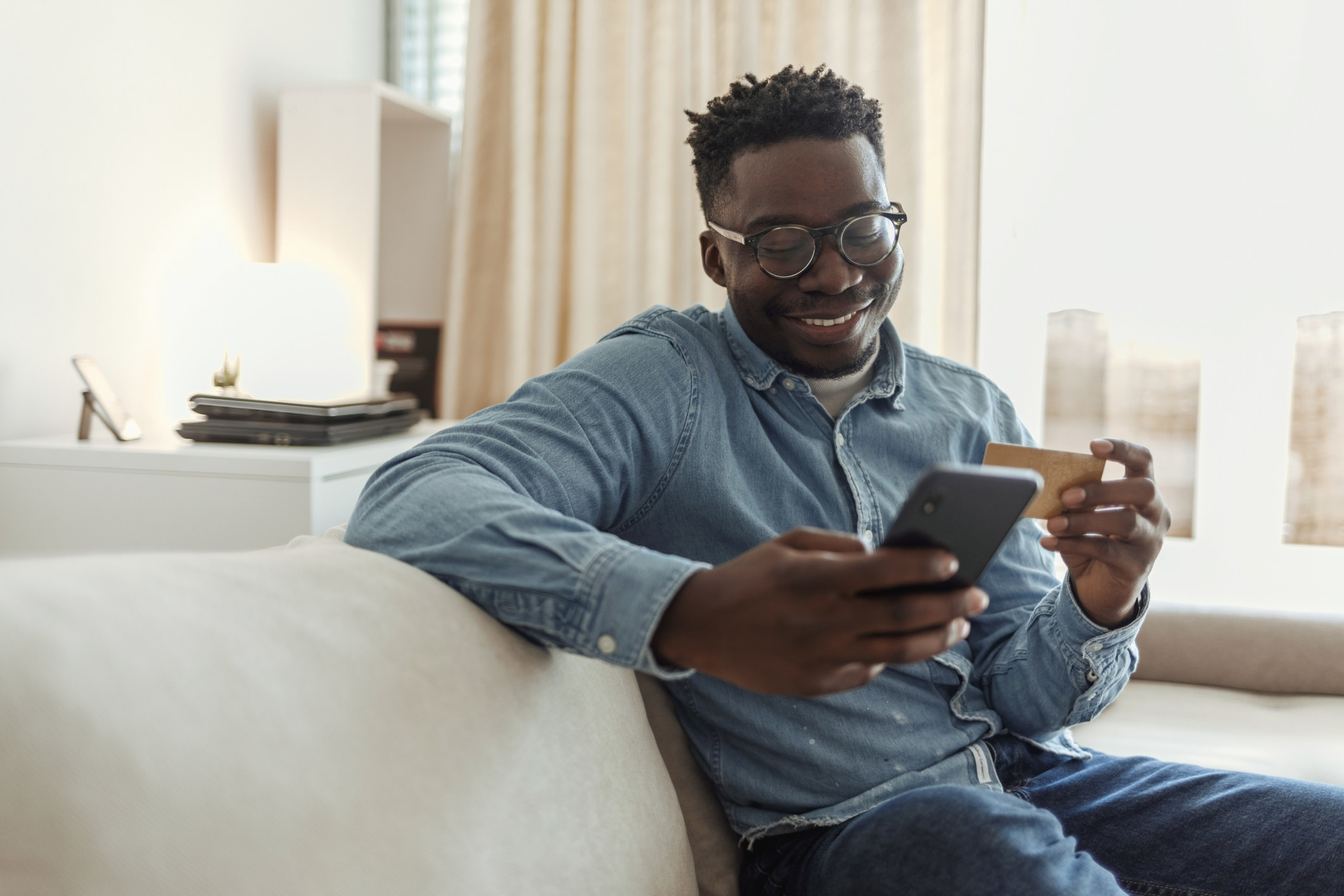 Shot of a young man holding his credit card while using a smartphone at home.