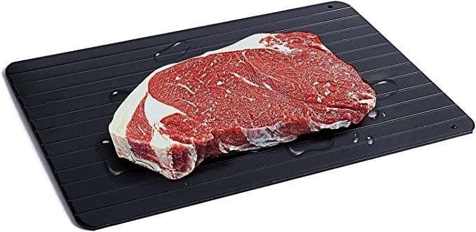 A picture of a defroster and cutting board with a slab of raw meat on it