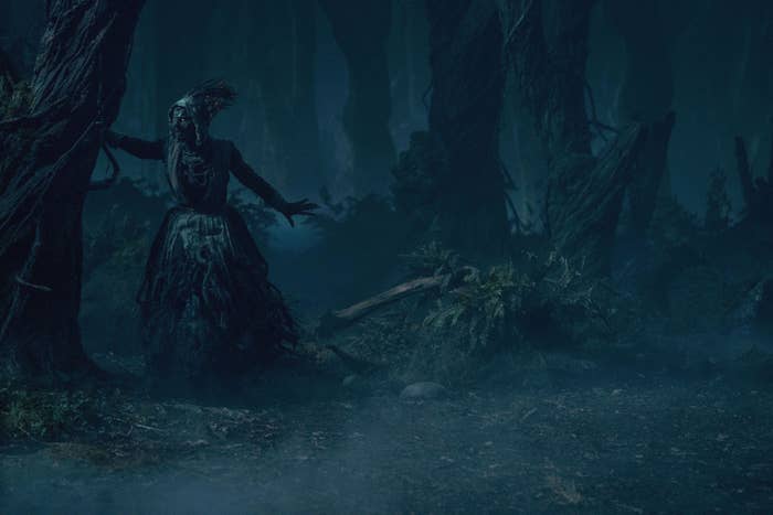A spooky witch holds her victim against a tree in a decrepit forest at night