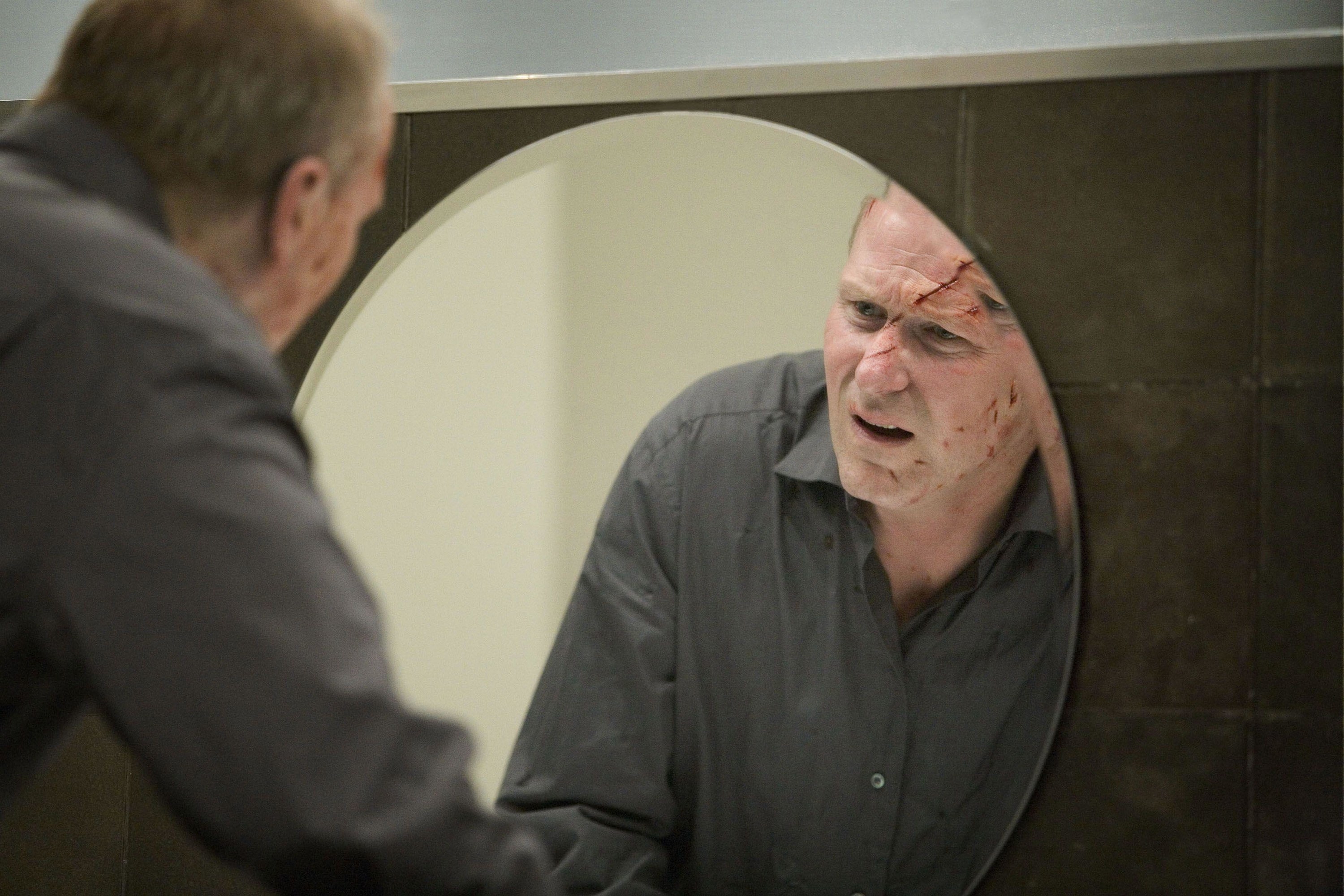 An injured man examines his facial wounds in a mirror