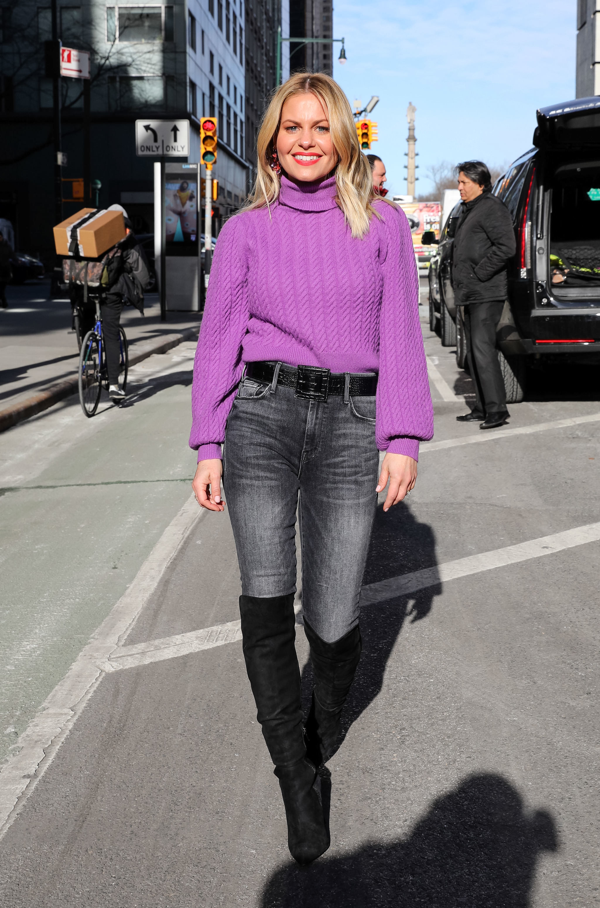 Candace smiles as she poses for a photograph in a long-sleeved sweater top and jeans and boots
