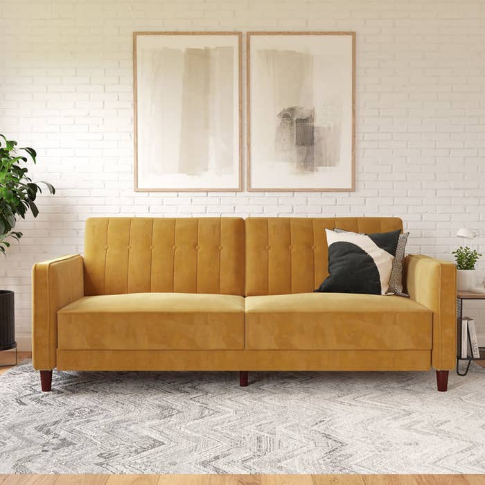 a yellow velvety sofa with a throw pillow on it