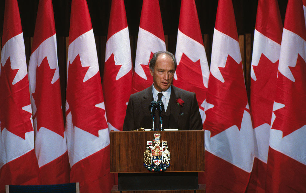 Pierre Trudeau, the Prime Minister of Canada making an address from a podium with Canadian flags in the background.