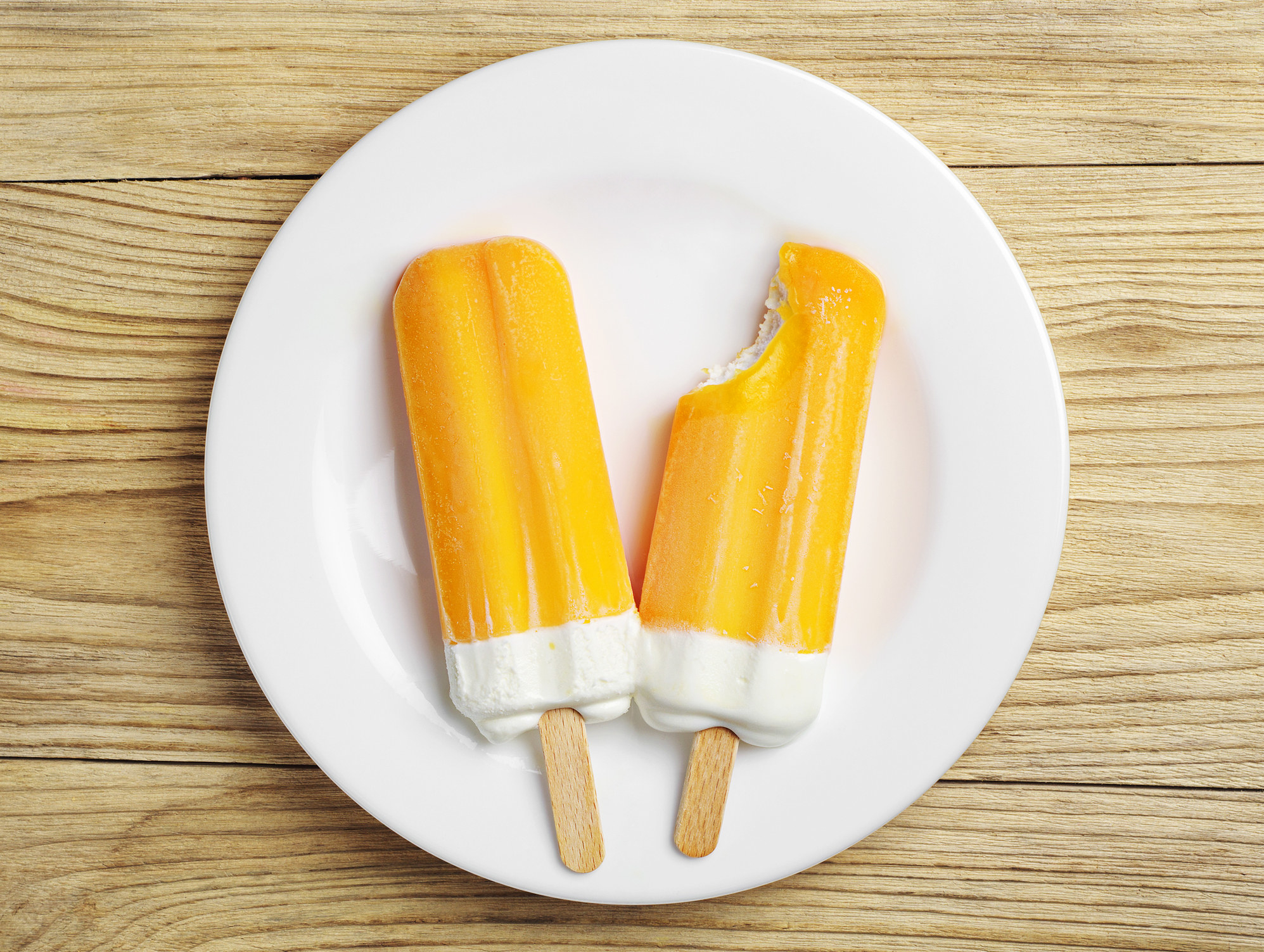 Two orange and cream ice pops on a plate.