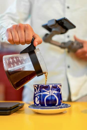 Person pouring coffee into a blue and white mug