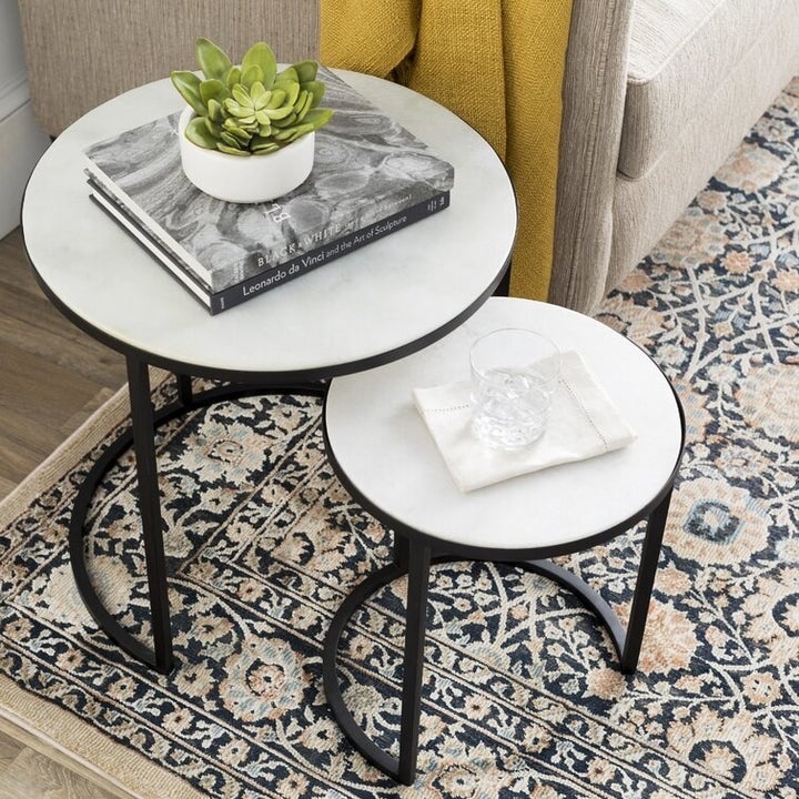 two black and white nesting tables with a drinking glass, books, and plant on them