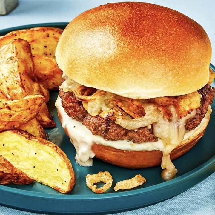 altın kızarmış patates dilimleri ve erimiş peynirle sızan burger ile bir tabak