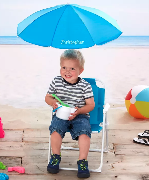 A kid sitting in a blue beach chair that says Christopher on the umbrella