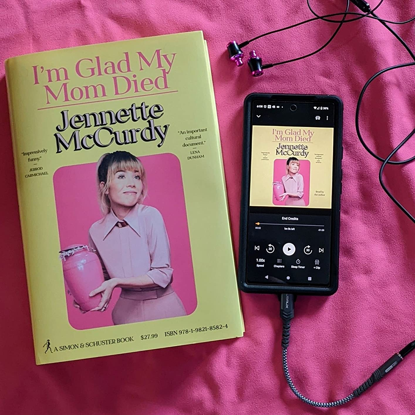 A copy of a book titled, &quot;I&#x27;m Glad My Mom Died&quot; sitting on a bed next to an android phone playing the same book on Audible
