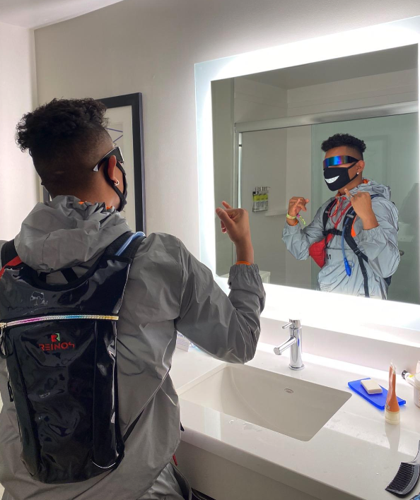 Boy looking at himself in mirror wearing hydration backpack. Photo taken of his back but his front is in view due to the reflection of the mirror.