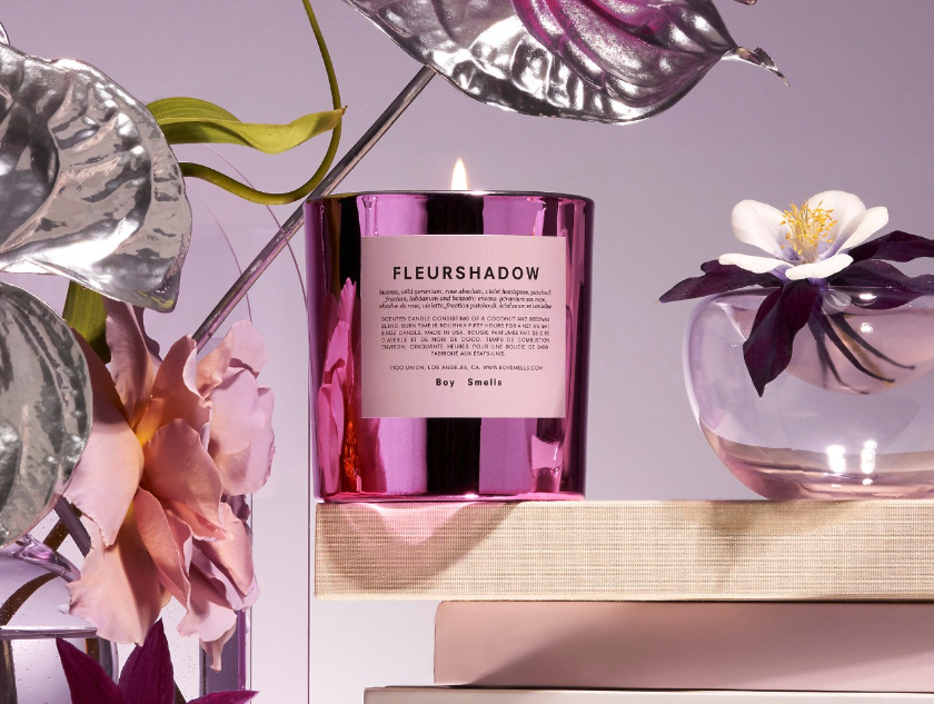 A candle with text reading &quot;fleurshadow&quot; on label, sitting on a ledge surrounded by flowers