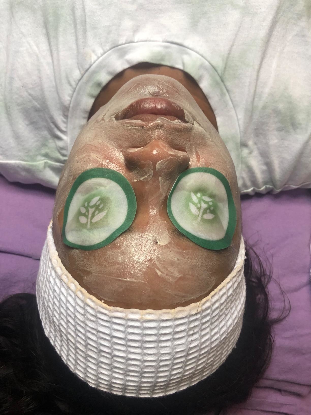 Reviewer getting a facial with cucumber pads on their eyes