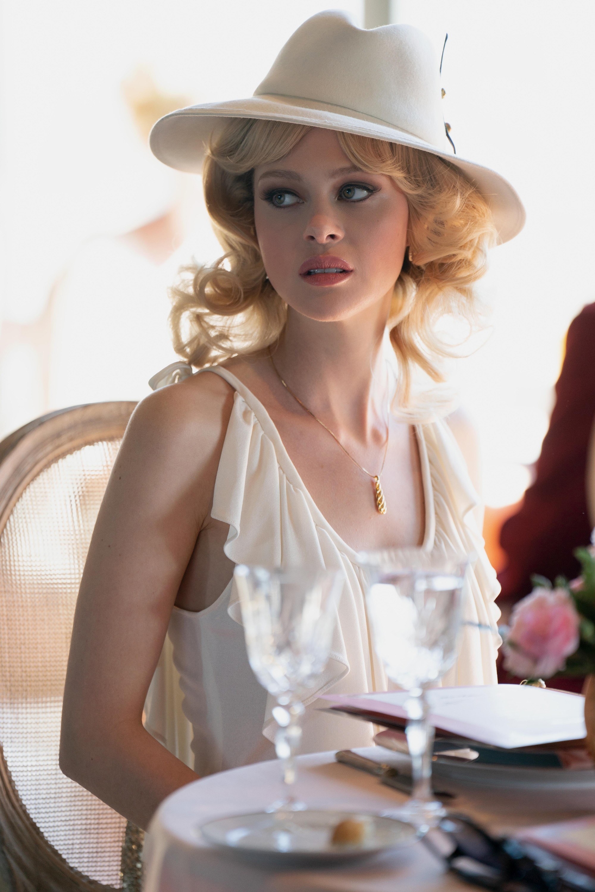 Dorothy wearing a flow-y outfit and a suede fedora as she sits in a restaurant in a scene from the miniseries