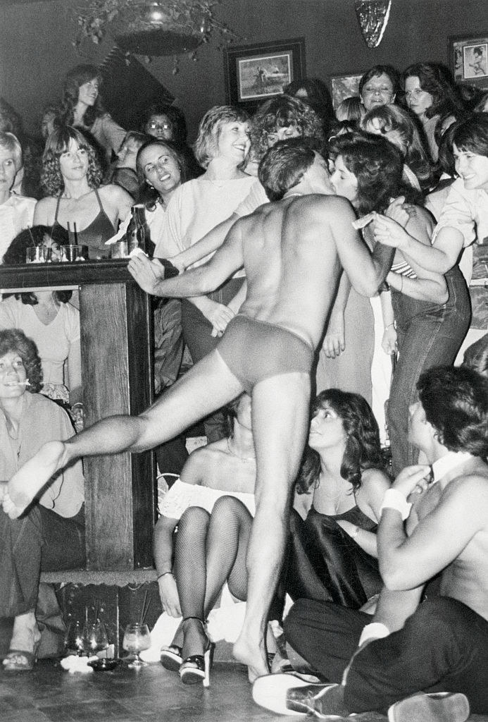 A Chippendales performing kissing a woman who&#x27;s surrounded by other women in the club