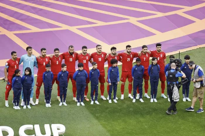 On a soccer field, a row of soccer players wearing red and children wearing blue stand together