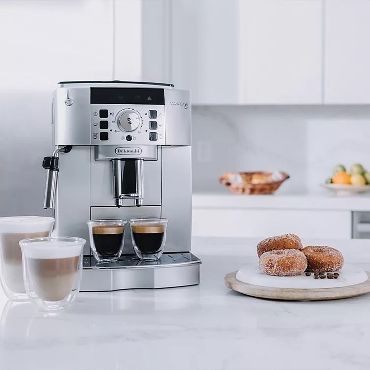 The cappuccino and espresso maker on a counter with four cups of coffee and three donuts near it.
