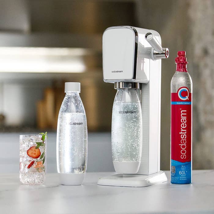 a soda stream with two bottles, a co2 canister and a glass of fizzy water