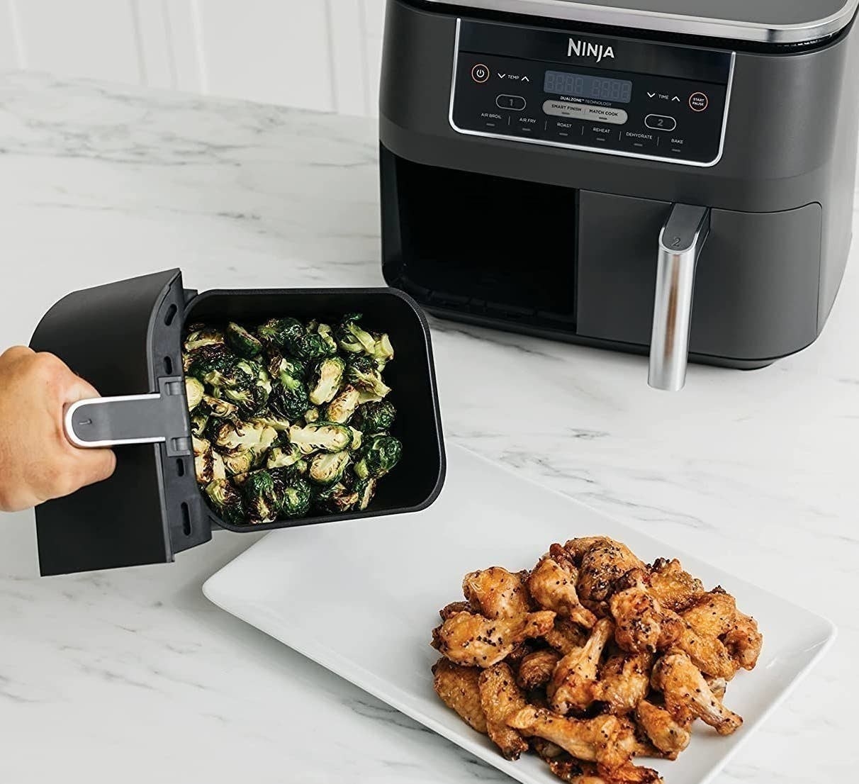 a person using the ninja air fryer to make two dishes simultaneously