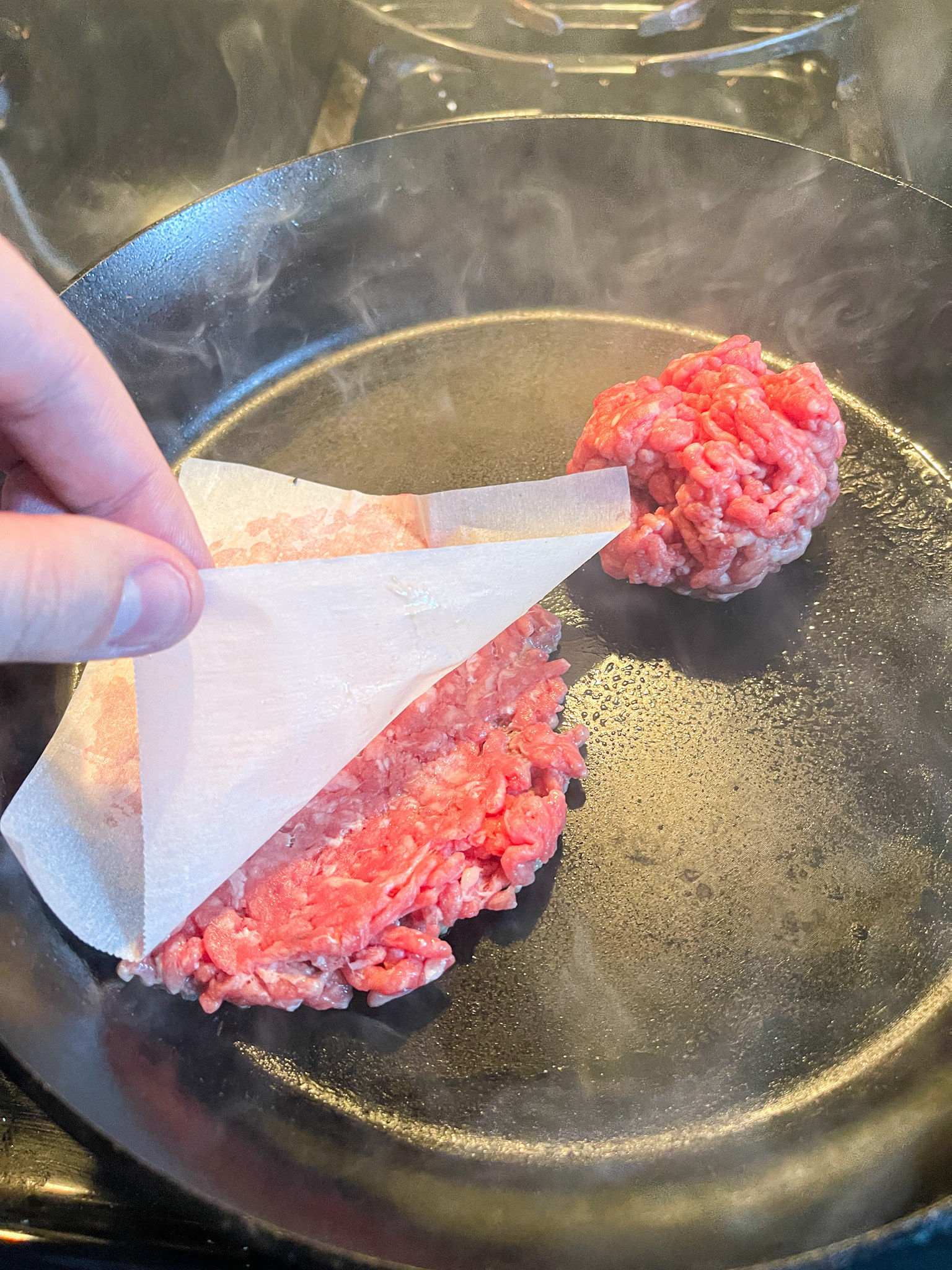 pulling parchment paper off of smashed burger on skillet