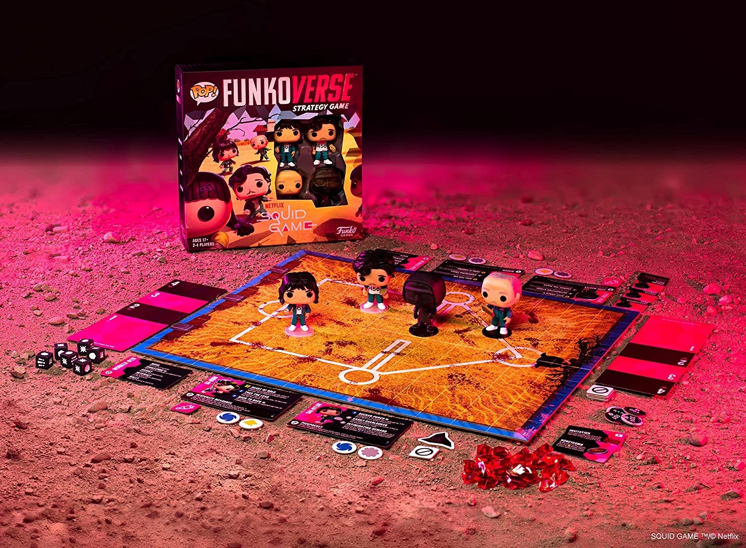 A boardgame that has the squidgame logo printed on it with lots of cards and pieces around the edge, and four of the funko characters on the board