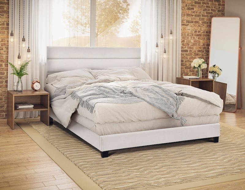 a cream colored upholstered bed with comfy looking blankets on it