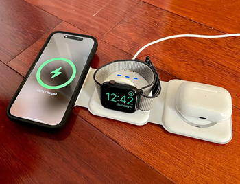 reviewer photo of a white charger pad laid out to charge a phone, watch, and AirPods