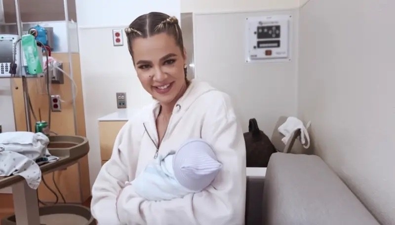 Khloé smiling and holding an infant