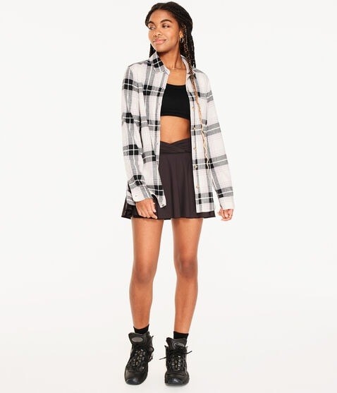 model wearing a black and white plaid button-down over a black crop top with a black mini skirt and sneakers