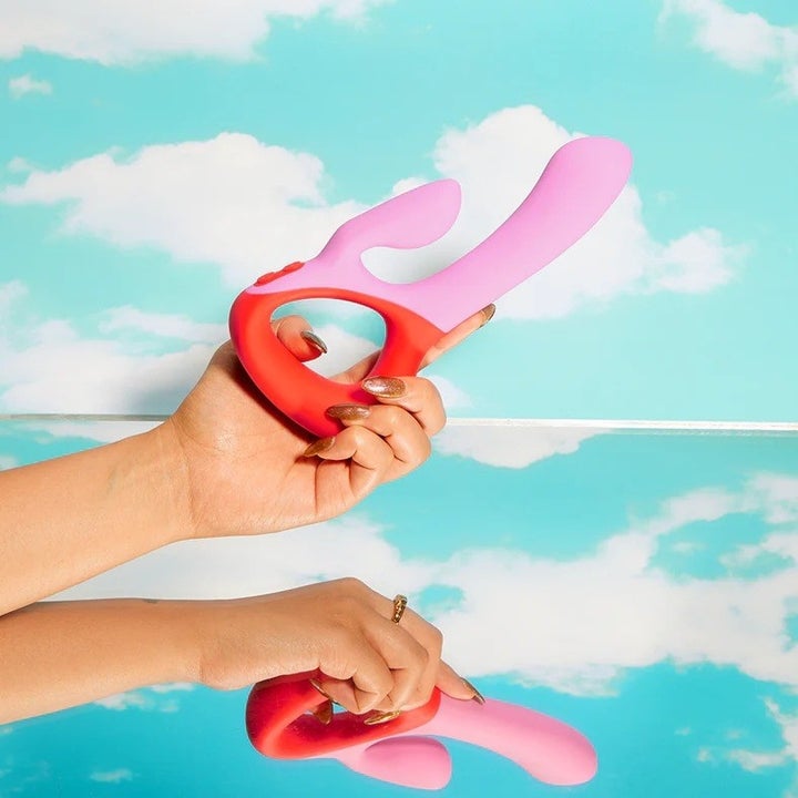 Hand holding pink and red dual-stimulating vibrator