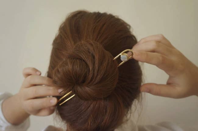 back of person's head with hair in bun held together with gemstone and gold hair stick