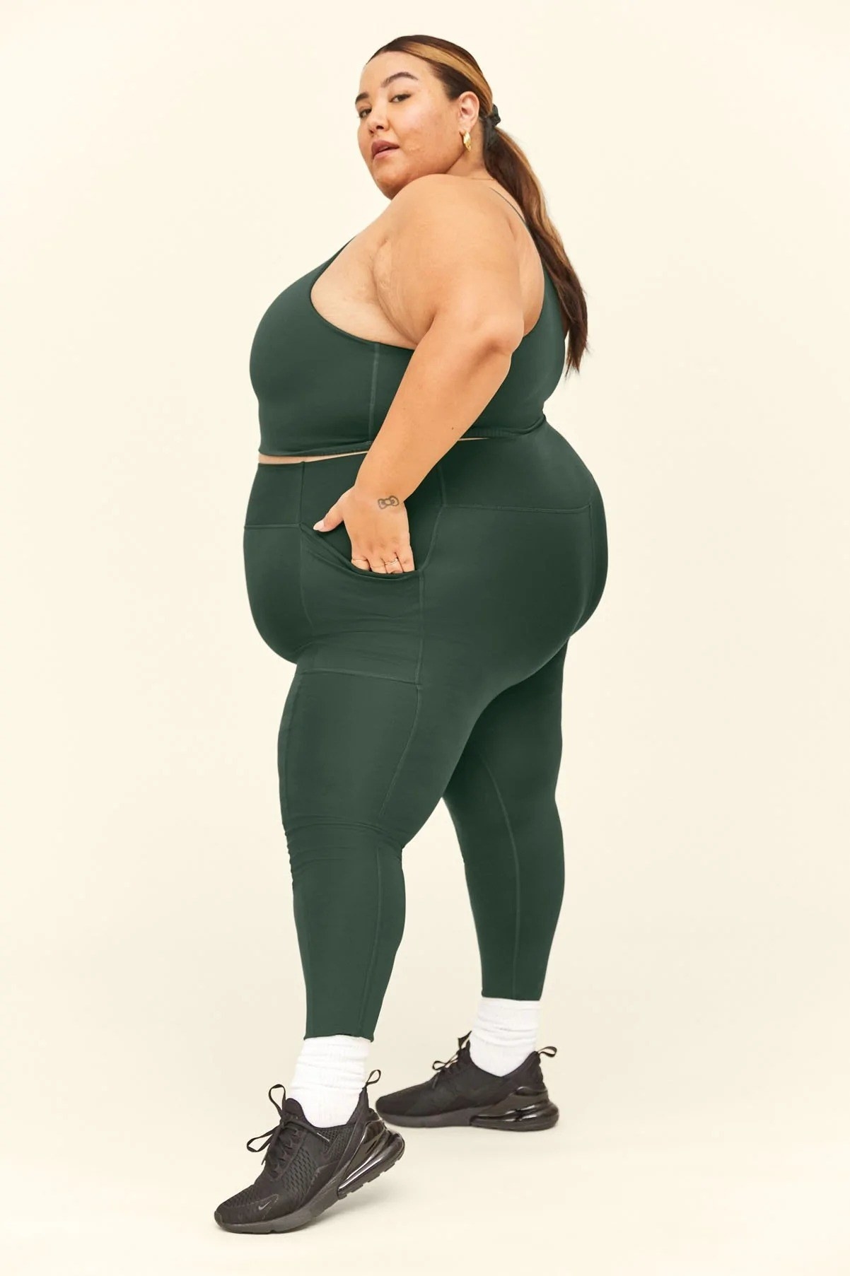 side view of model wearing the green pocket leggings with a matching sports bra, white socks, and black sneakers