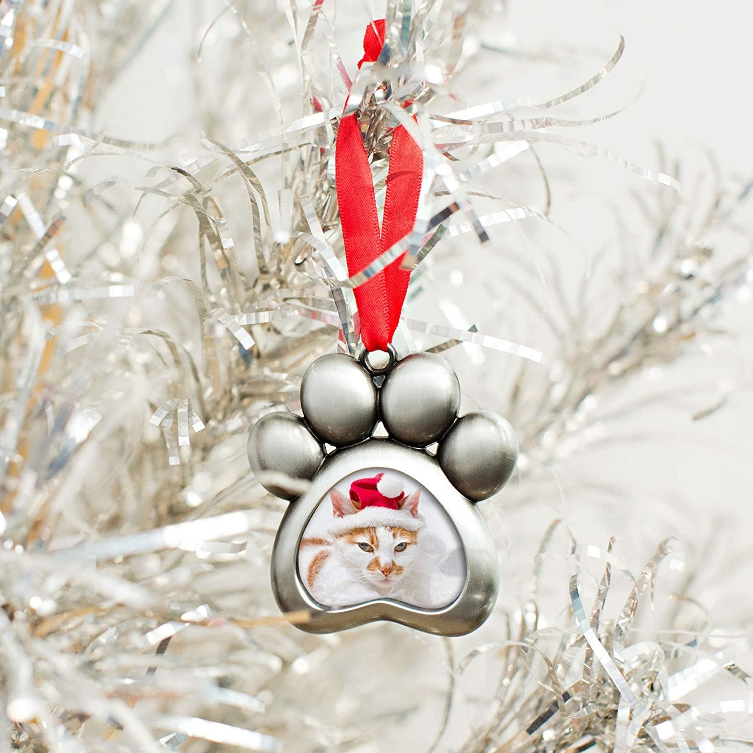 A paw-shaped hanging ornament containing a photo of a cat wearing a Santa hat