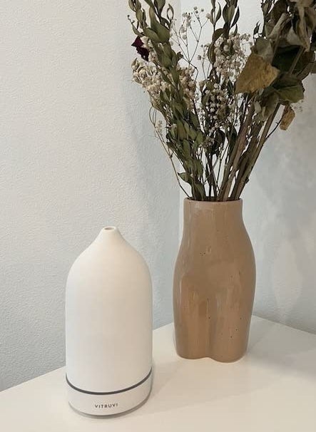 reviewer photo of a cream-colored diffuser next to a flower arrangement in a vase